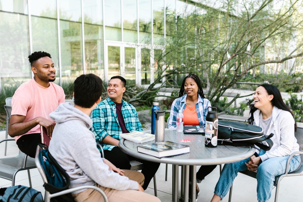 Diverse group of international students sitting around a table outside a campus building.